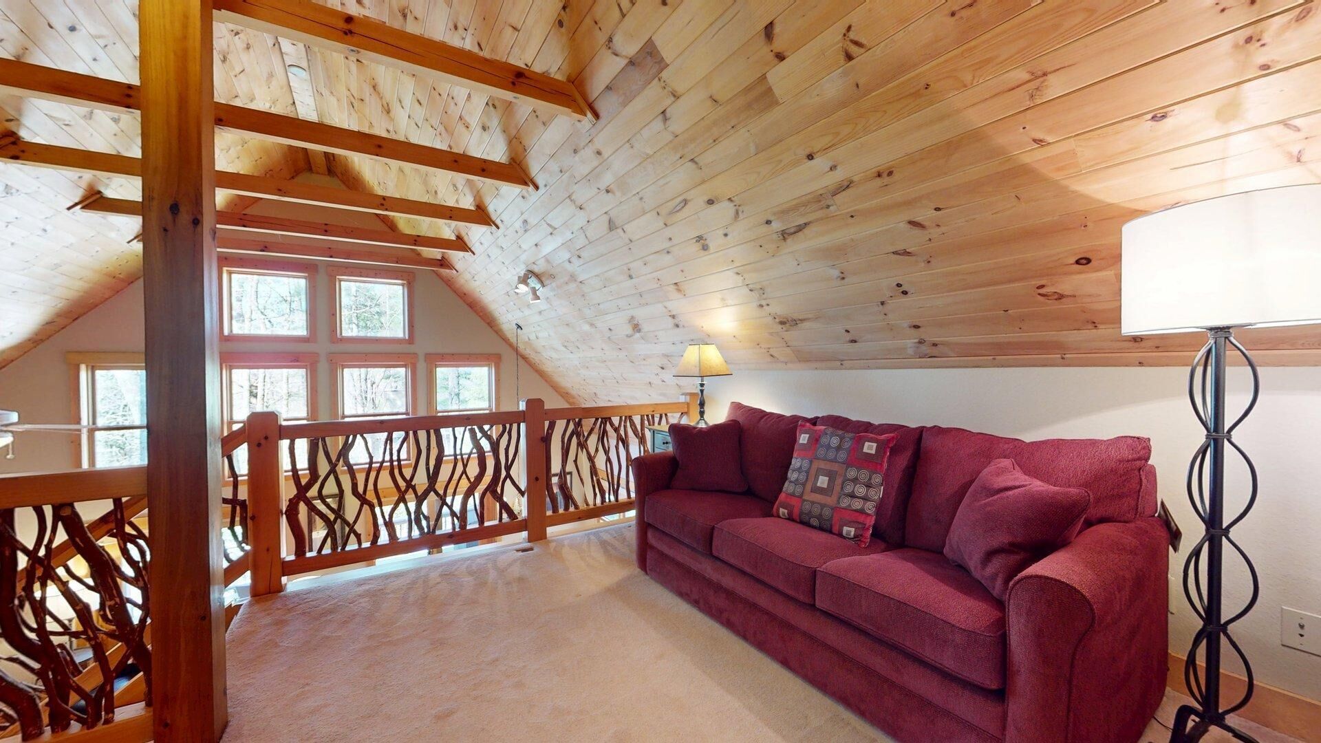 A cozy room with a wooden ceiling, a red sofa, and a windowed balcony.