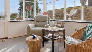 Ein Wintergarten mit einem Stuhl, einem Tisch und einem Korbwannen.