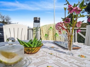 Une table avec un saladier en verre contenant des haricots verts, un verre rempli d’un liquide jaunâtre et un vase avec des fleurs roses.