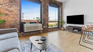 Een moderne woonkamer met met bakstenen accentmuren, grote ramen, een flatscreen televisie, een bank, een salontafel en een tv-meubel.