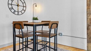 Een eetruimte met een ronde tafel, vier houten stoelen, een wandklok en een vloerlamp.