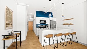 A modern kitchen with white cabinetry, a central island with bar stools, and a blue accent wall. - Duluth Craft Loft | Dog-Friendly (Duluth)