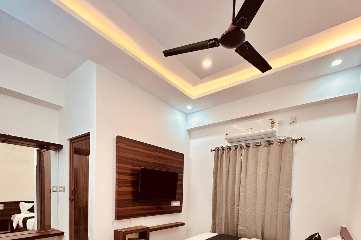 A modern bedroom with a bed, a ceiling fan, a mounted TV, and a bathroom with a shower and toilet.