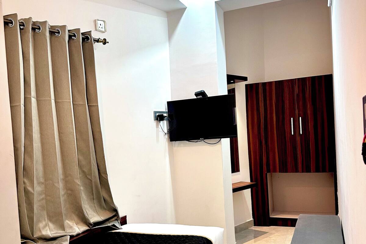 A bedroom with a bed, a TV mounted on the wall, a wardrobe, and a small seating area.