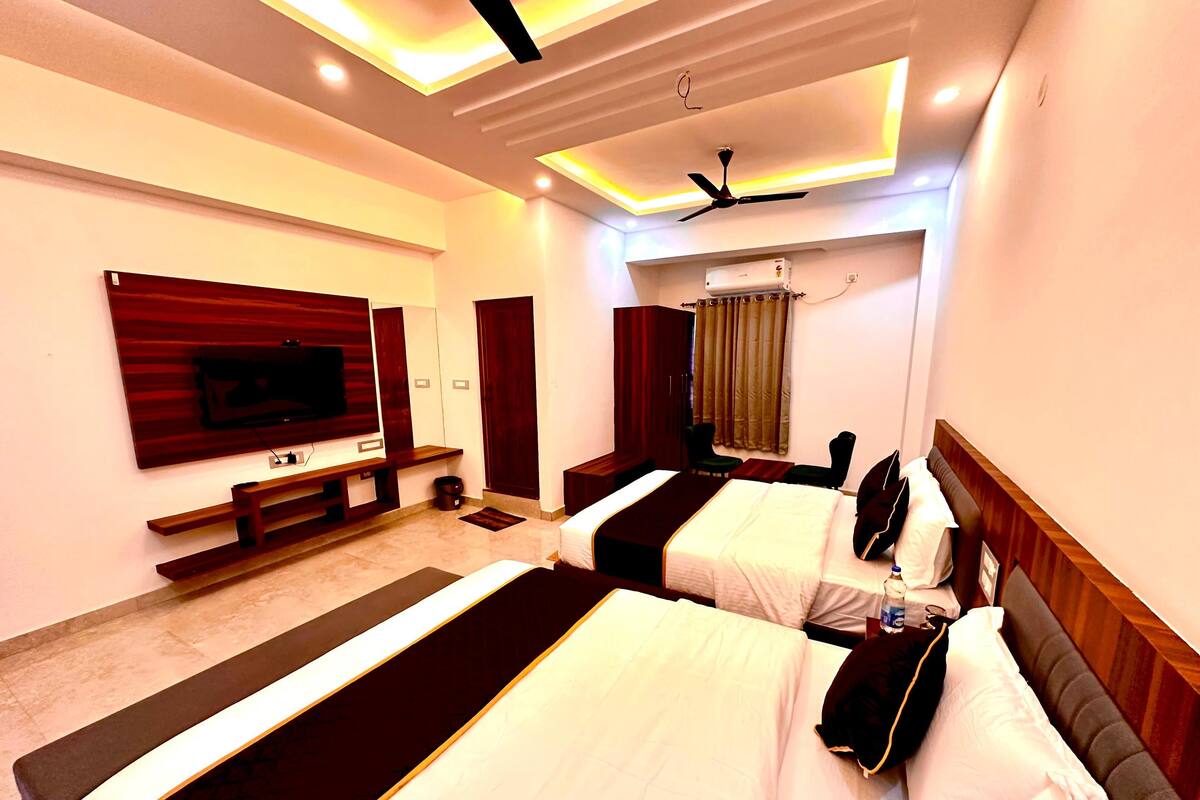 A hotel room with two beds, a TV, a ceiling fan, and a window with curtains.