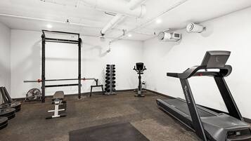 A gym with a treadmill, weight bench, squat rack, and various weights.