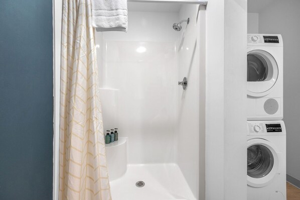 A bathroom with a shower, a toilet, and stacked washing machines.