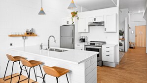 A modern kitchen with white cabinetry, a central island with bar stools, a built-in oven, and a coffee maker. - Craft District Apt w/ Gym & Coffee Shop 323 (Duluth)