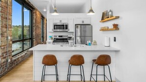 A modern kitchen with white cabinets, stainless steel appliances, and a central island with bar stools. - Craft District Apt w/ Gym & Coffee Shop 207 (Duluth)