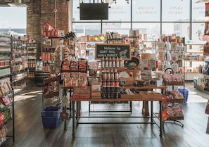 Interior de una tienda con estantes repletos de diversos productos alimenticios y un letrero de bienvenida al Gat Hill World Market.
