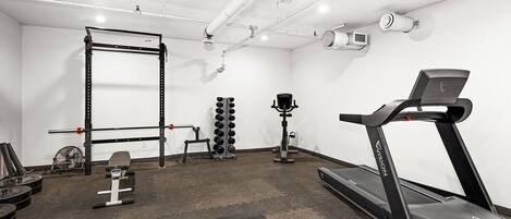A gym with a treadmill, weight bench, squat rack, and various weights.
