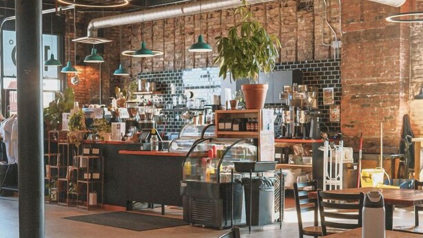 A spacious cafe with exposed brick walls, industrial-style lighting, and a variety of seating options including tables and chairs. - Craft District Apt w/ Gym & Coffee Shop 223 (Duluth)