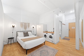 Un dormitorio moderno con cama, lavadora y una pequeña mesa.