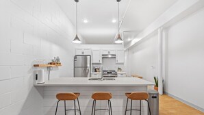 A modern kitchen with white cabinetry, a central island with bar stools, stainless steel appliances, and pendant lighting. - Craft District Apt w/ Gym & Coffee Shop 223 (Duluth)