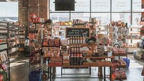 A grocery store with a variety of products on shelves and tables, a sign reading "Welcome to Got Hill World Market," and a brick wall on one side. - Craft District Apt w/ Gym & Coffee Shop 223 (Duluth)