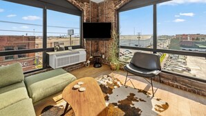 Een moderne woonkamer met grote ramen, een flatscreen televisie, een bank, een stoel en een klein tafeltje.