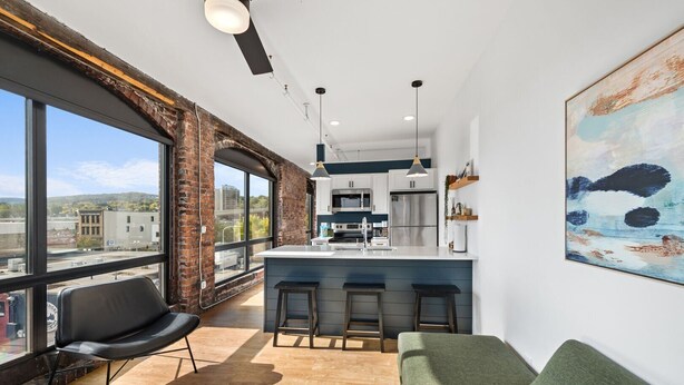 Een moderne keuken met een groot eiland, barkrukken en uitzicht op de stad door grote ramen.