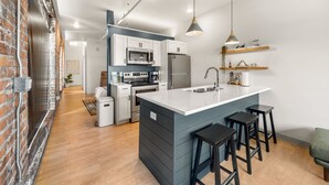 Een moderne keuken met een groot kookeiland, roestvrijstalen apparatuur en een accentmuur van baksteen.
