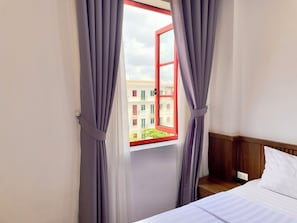 A hotel room with a bed, a wooden headboard, and a window with curtains. - KIEN HOTEL (Phu Quoc)