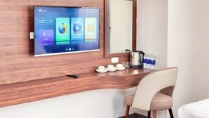 A hotel room with a mounted TV displaying a home screen, a wooden desk with a kettle, cups, and a chair. - KIEN HOTEL (Phu Quoc)