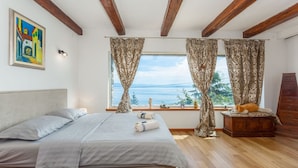 Un dormitorio con cama, cortinas, cómoda, un cuadro y ventana con vistas.