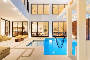 A spacious indoor pool area with a hammock, seating, and a view of the kitchen and dining area.