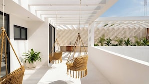 Un intérieur moderne avec un plafond blanc, des fauteuils suspendus en osier et une vue sur un jardin grâce à de grandes fenêtres.
