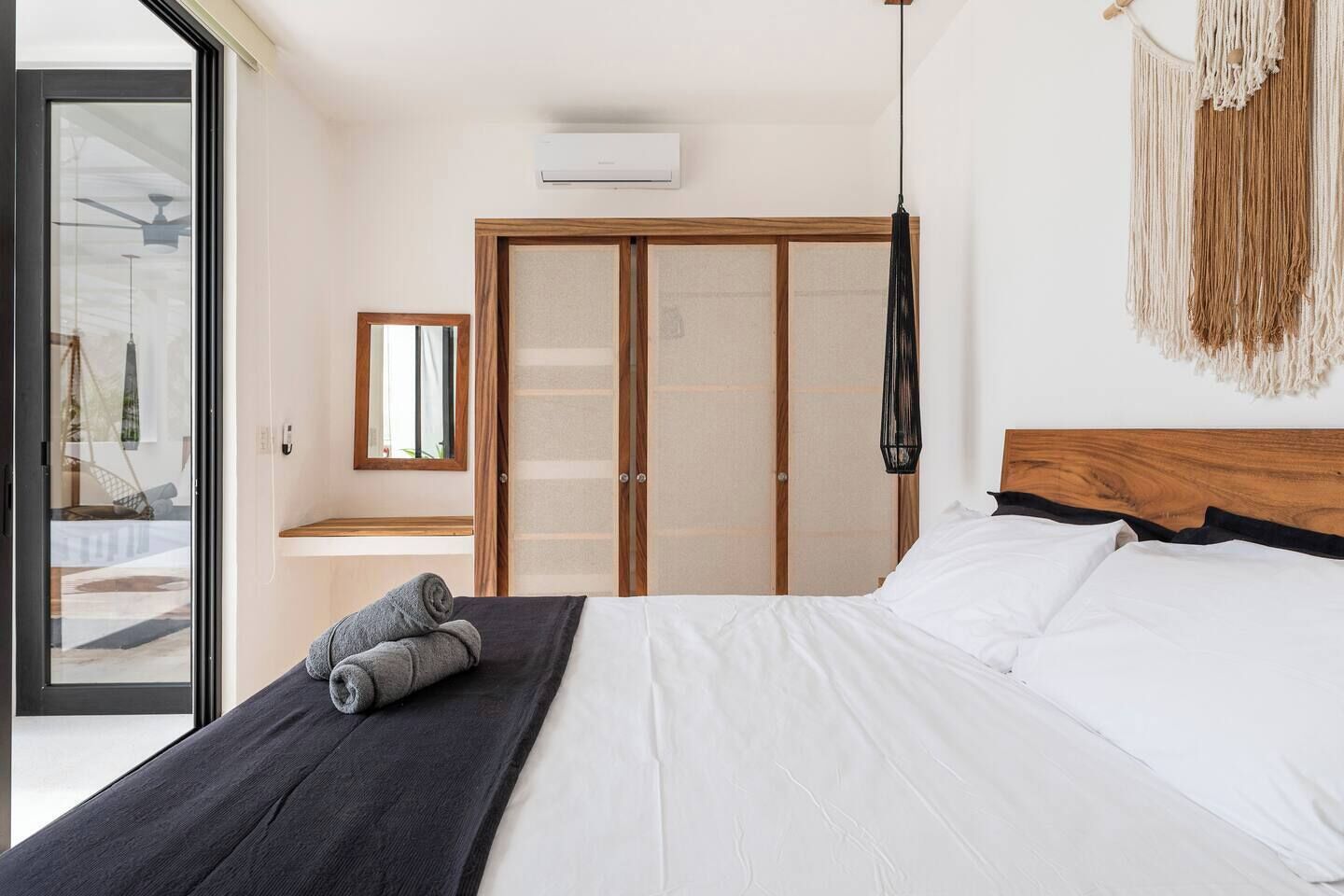 Una camera da letto con un letto, una testata in legno, una lampada appesa in macramè e un armadio a ante scorrevoli.