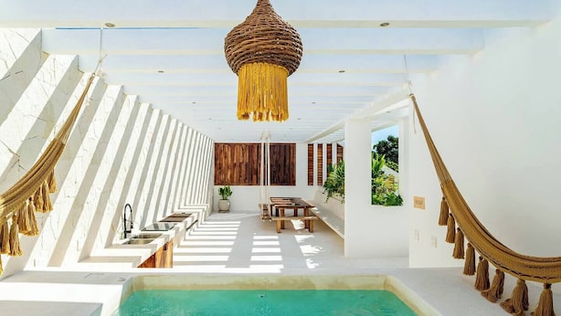 Un espace piscine moderne offrant une vue dégagée sur la piscine, avec un banc en bois et un luminaire suspendu.