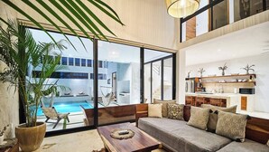 A modern living room with a sofa, coffee table, and a view of a swimming pool. - New Spacious Villa with Rooftop dipping pool (Tulum)