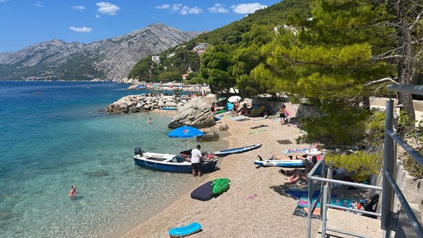 A beach with clear water, boats, umbrellas, and people.