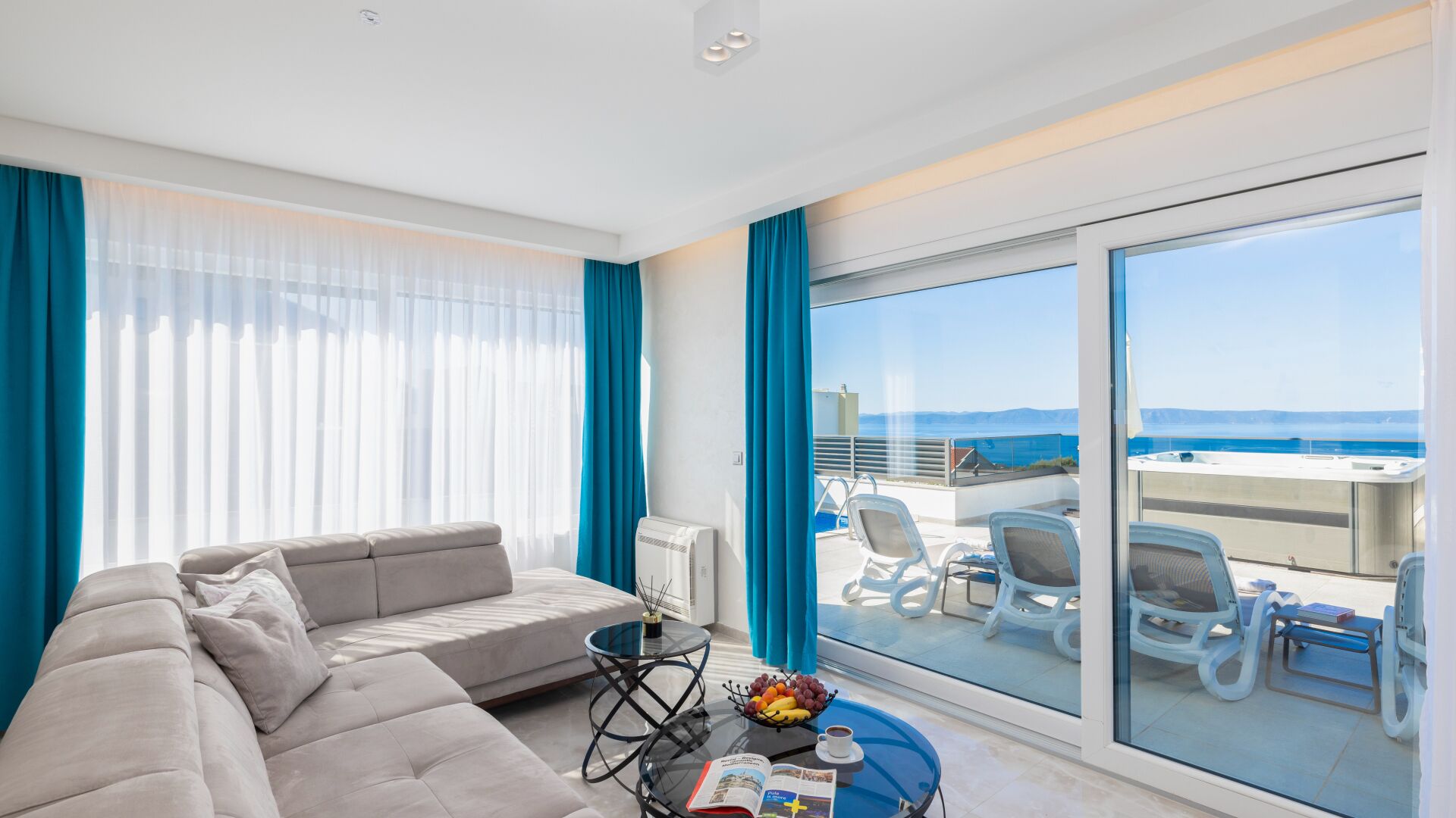 A modern living room with a sofa, a glass coffee table, and a view of the sea through large windows.