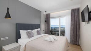 Una habitación de hotel moderna con una cama grande, un televisor de pantalla plana, un balcón con vistas al mar y un diseño minimalista.