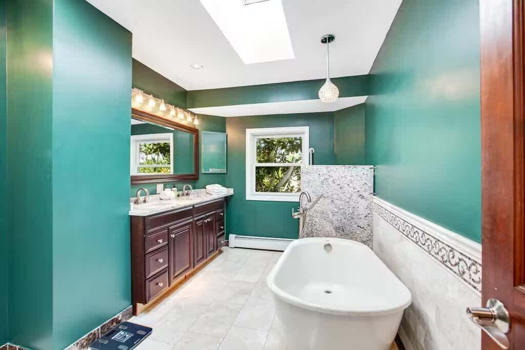 A bathroom with teal walls, a freestanding bathtub, dark wooden cabinets, and a window providing natural light.