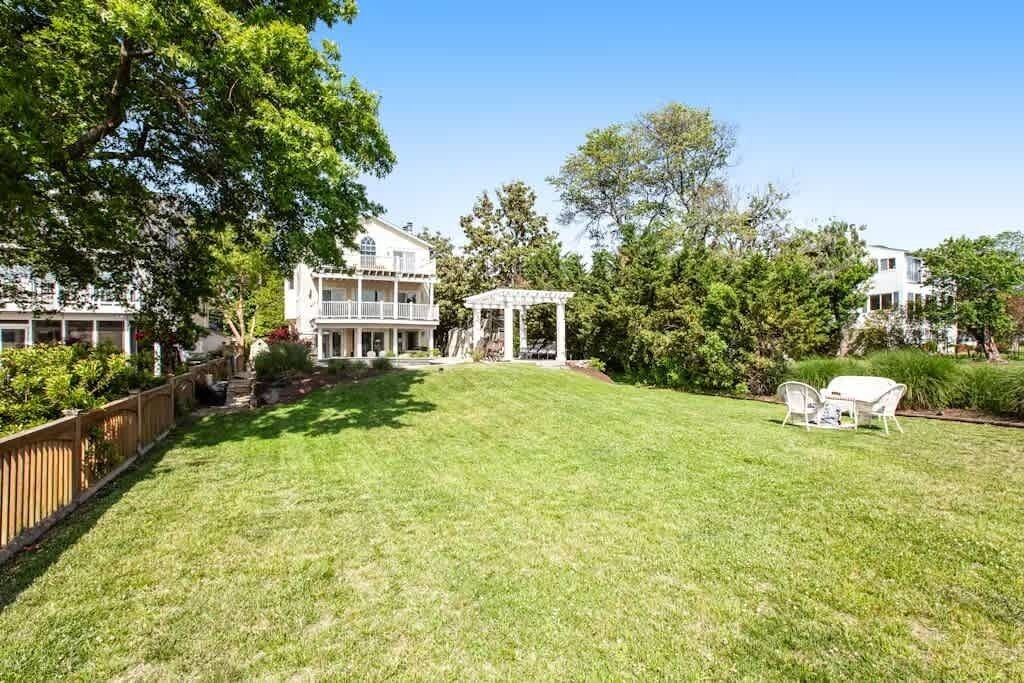Un patio amplio con una pérgola, una zona de estar exterior blanca y un césped bien cuidado.