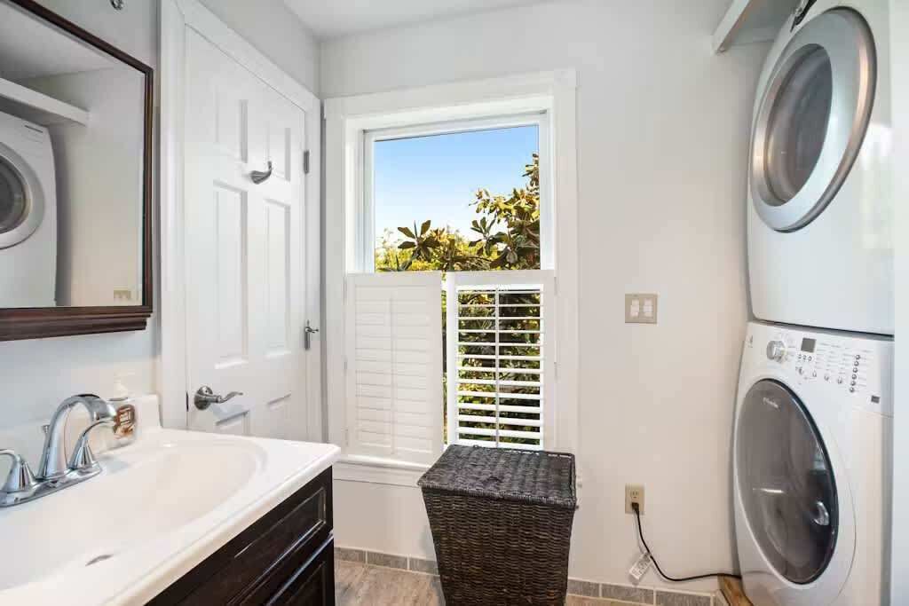A laundry room with a washing machine, a dryer, a sink, and a window with blinds.