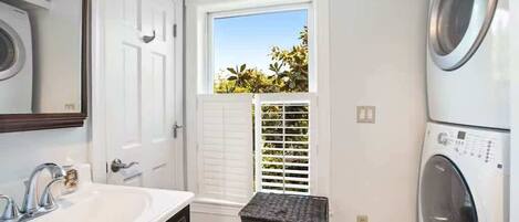 A laundry room with a washing machine, a dryer, a sink, and a window with blinds.
