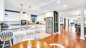 Une cuisine moderne avec des meubles blancs, des appareils en acier inoxydable et une table à manger en bois, assortie de chaises blanches.