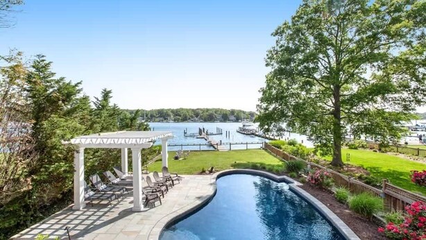 Une piscine agrémentée d’une pergola et de chaises longues, entourée d’un jardin aménagé et offrant une vue sur un lac.