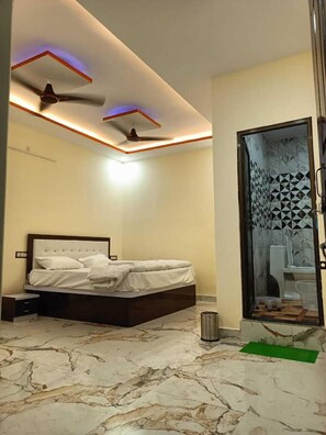 Ein Schlafzimmer mit Bett, Deckenventilator und einem Badezimmer mit Toilette und Dusche.