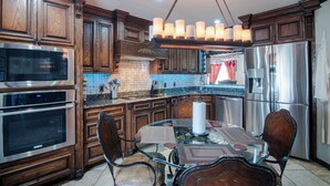 A kitchen with wooden cabinets, stainless steel appliances, a glass dining table, and a hanging light fixture. - Charming Pond Villa 3-bedroom 2 Bath house DFW (Grand Prairie)