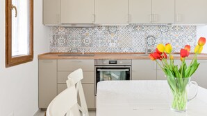 Een keuken met lichte kastjes, een decoratieve spatwand en een glazen vaas met tulpen op het aanrecht.