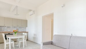 Een moderne keuken met witte kastjes, een eettafel met stoelen en een grijze bank.