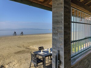 A beach view from a covered patio with a table and chairs, overlooking the beach and a distant mountain range. - Sogno di Mare by Interhome (Follonica)