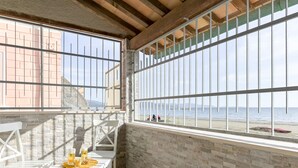 Een balkon met witte stoelen en een tafel, met uitzicht op een strand en een helder zicht op de zee en verre bergen.