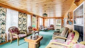 A cozy room with wooden floors, floral curtains, wicker furniture, and a glass coffee table. - Creekside Retreat in the Adirondacks: Swim & Hike! (Forestport)