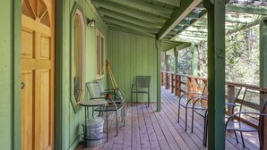 A green wooden porch with a wooden door, metal chairs, a small table, and a metal bucket. - Walk to Dining! Peaceful Arnold Cabin w/ Deck (Arnold)