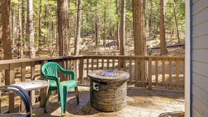 A deck with a stone fire pit, a table, and two chairs, surrounded by a forest. - Hike, Ski & Sip: Arnold Cabin 4 Mi to State Park! (Arnold)