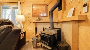 A cozy room with a wooden interior, a fireplace, a sofa, a lamp, and a window. - Hike, Ski & Sip: Arnold Cabin 4 Mi to State Park! (Arnold)