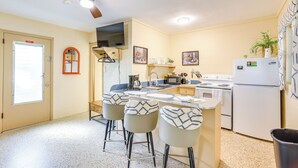 A compact kitchen with a central island, bar stools, a ceiling fan, and a refrigerator. - Lanai & Fire Pit: Riverfront Studio in Chiefland! (Chiefland)